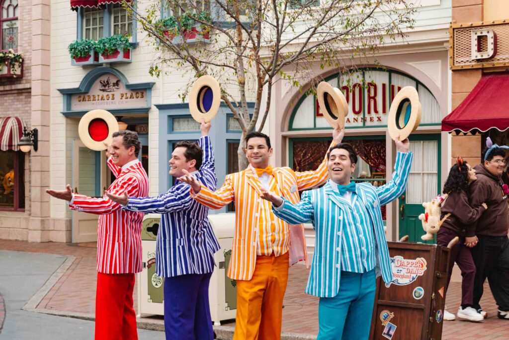Singing barbershop quartet dressed in red, purple, yellow, and blue pinstripe suits with matching colorful hats on Main Street USA in Disneyland also known as the Dapper Dans