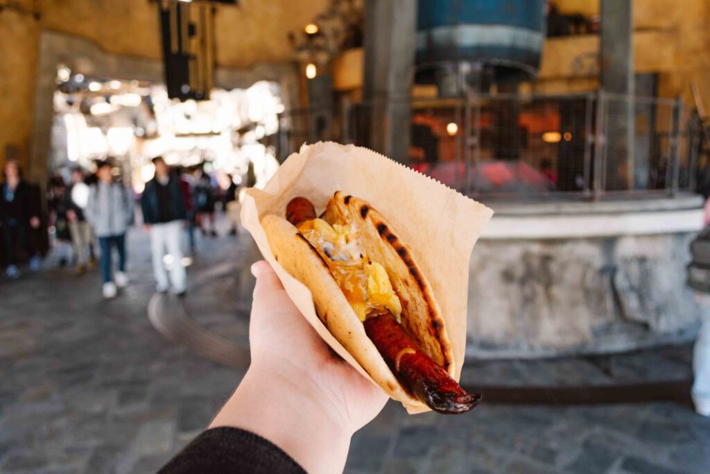 Galaxy's Edge ronto wrap for breakfast being held by a woman's hand outstretched from the camera with a Star Wars machine in the background