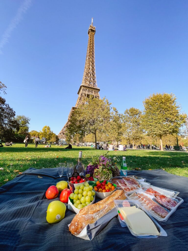 Picnic at the Eiffel Tower on the grass out front with a baguette, fruit, meats, and cheeses.