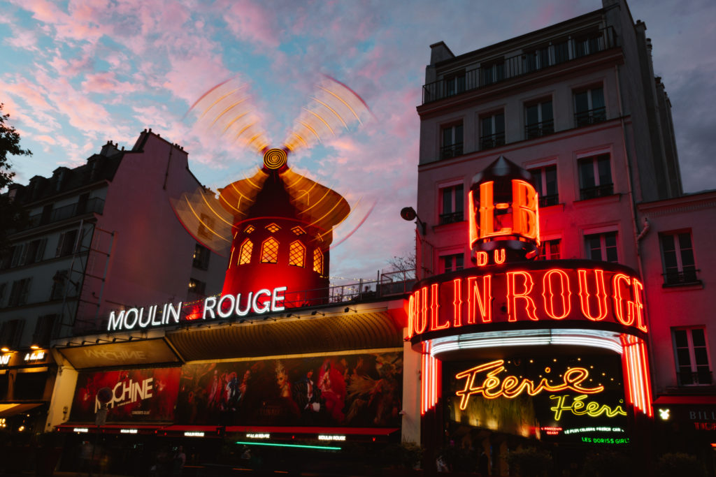 Moulin Rouge lit up during sunset with blue sky and small pink clouds